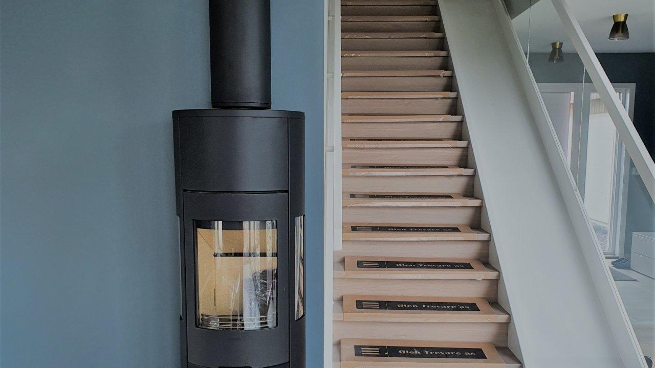 A black wood stove on a steel chimney beside a staircase