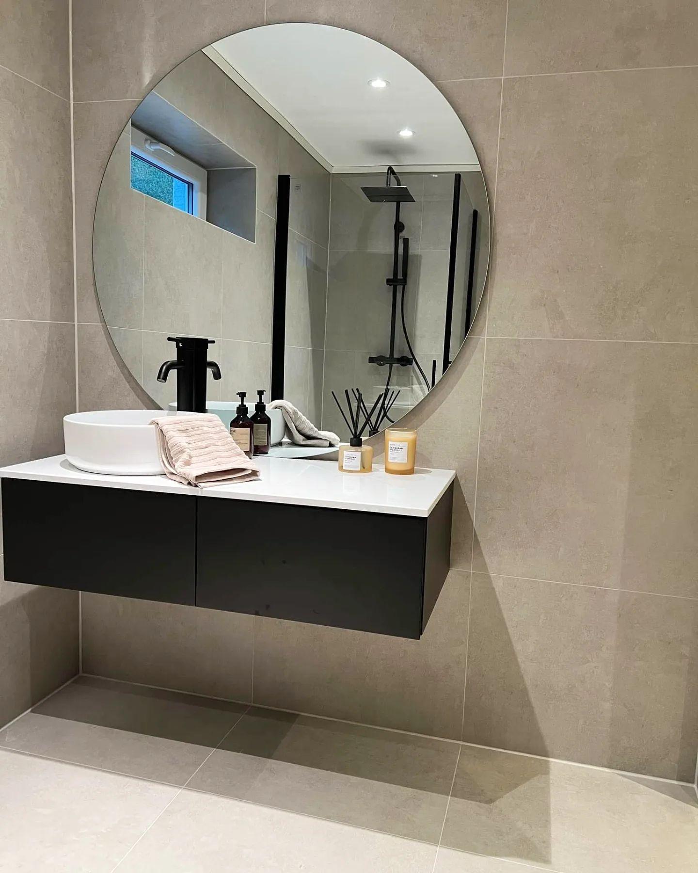 A black vanity with a round mirror against pale tiles