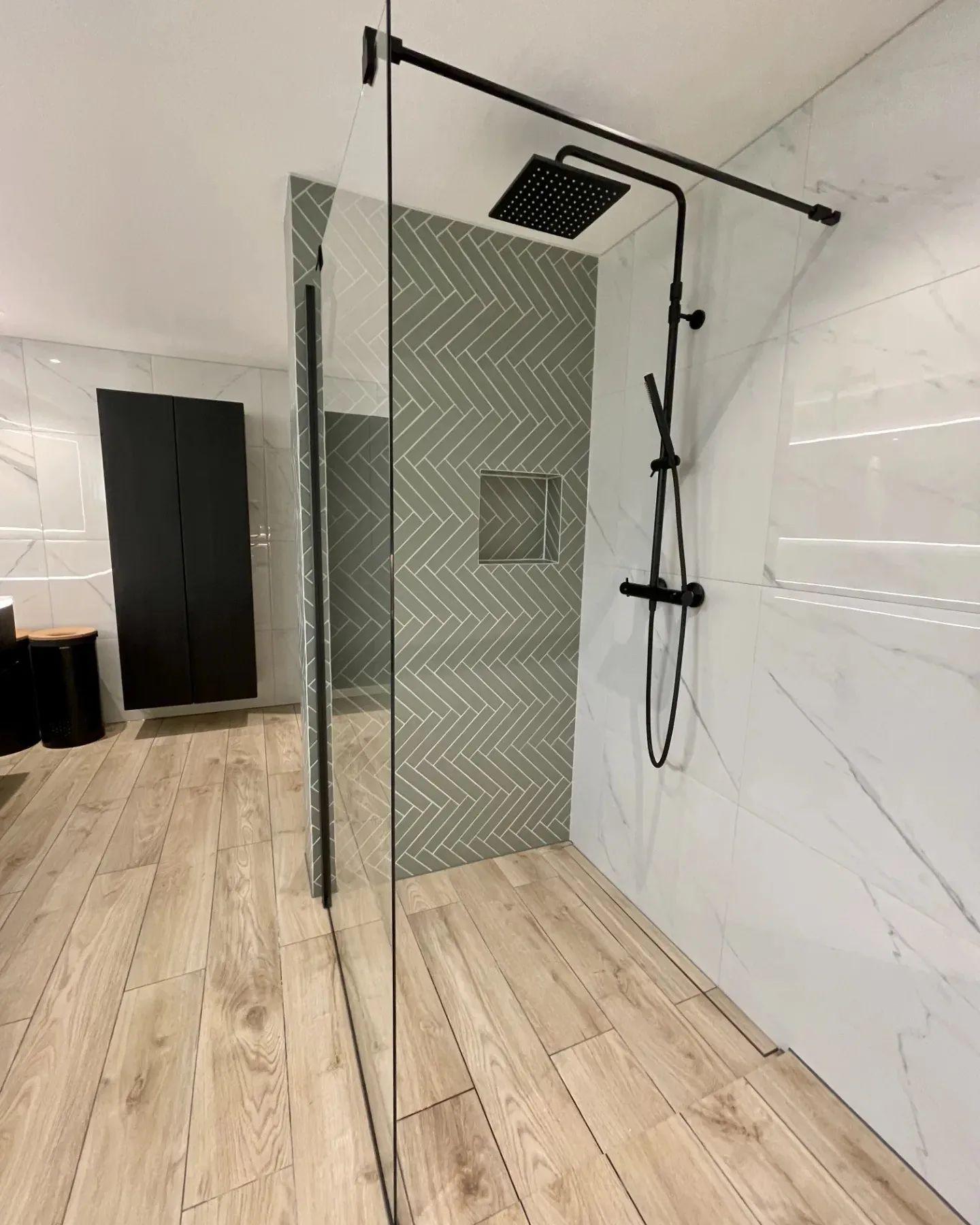 A walk-in shower behind a glass screen, with a wood-look tiled floor