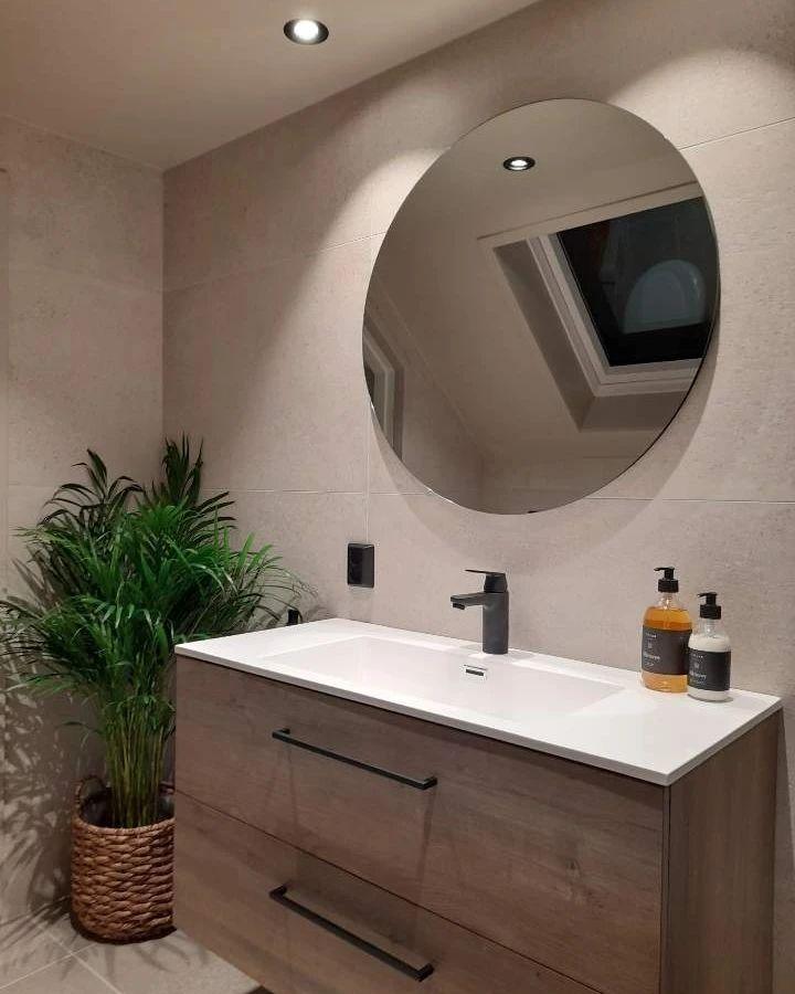 A wooden vanity with a round mirror and a plant