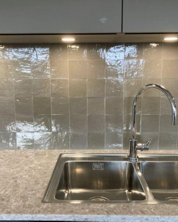 A kitchen with a steel sink and a tiled splashback