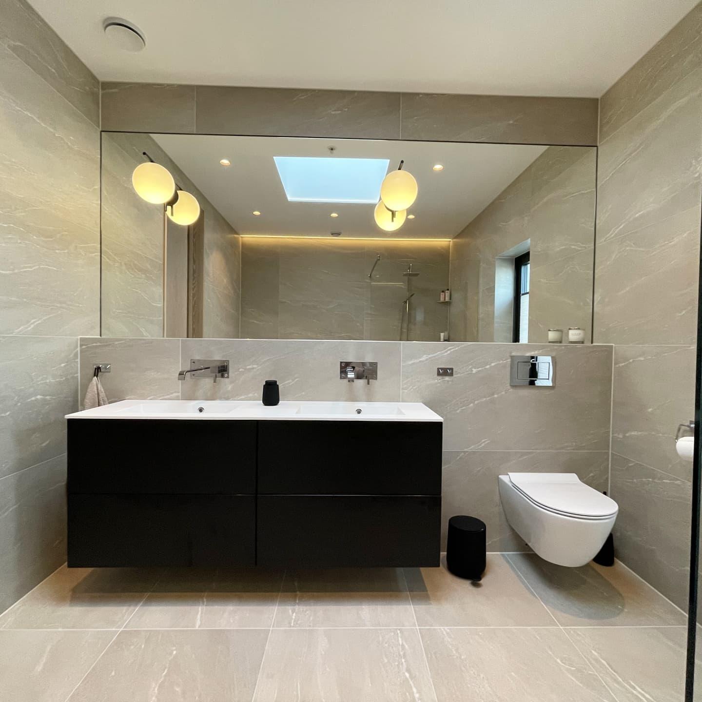 A bathroom with a double black vanity, round mirrors and a skylight