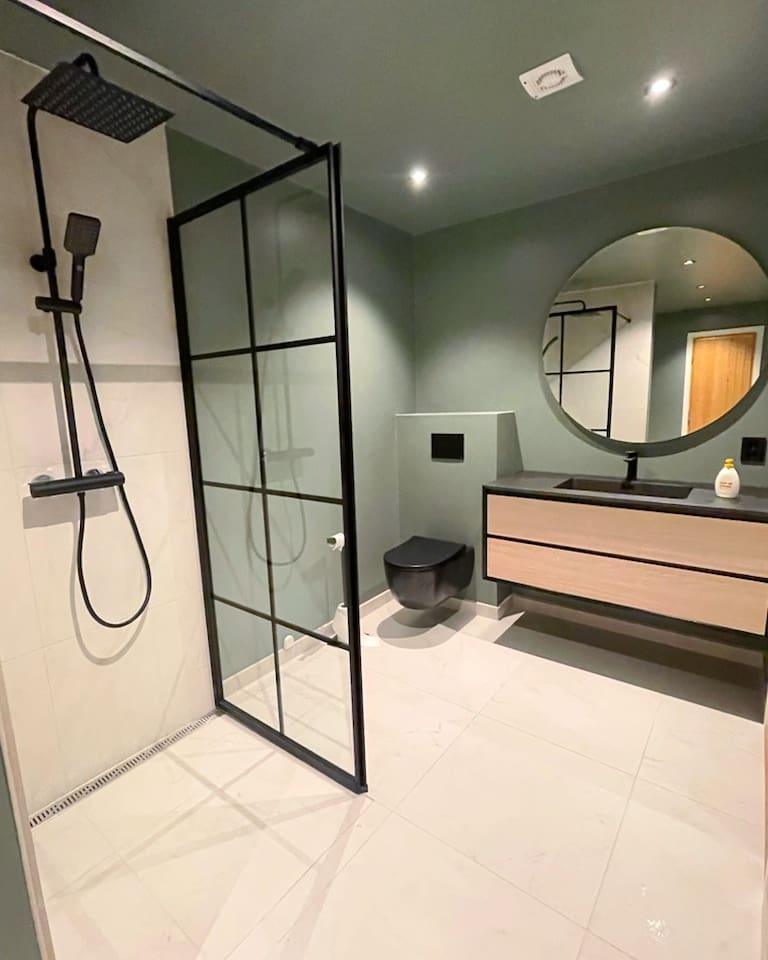 A shower behind a black framed screen, with a wood vanity beyond