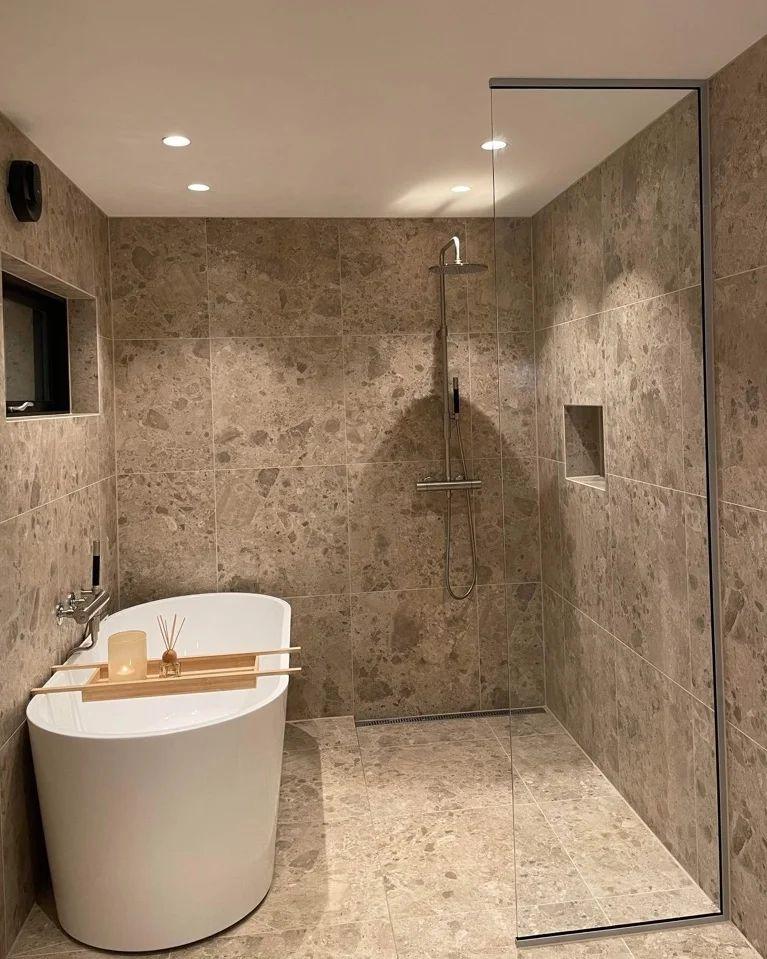 A shower in terrazzo-look tiles beside a freestanding bath